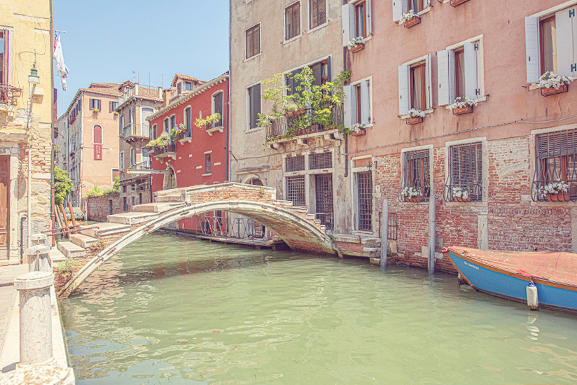 Photo of Pont Chiodo, the last bridge in Venice with no parapet. The canal has flowing green water and is set against a backdrop of colourful houses. This is an authentic travel experience.