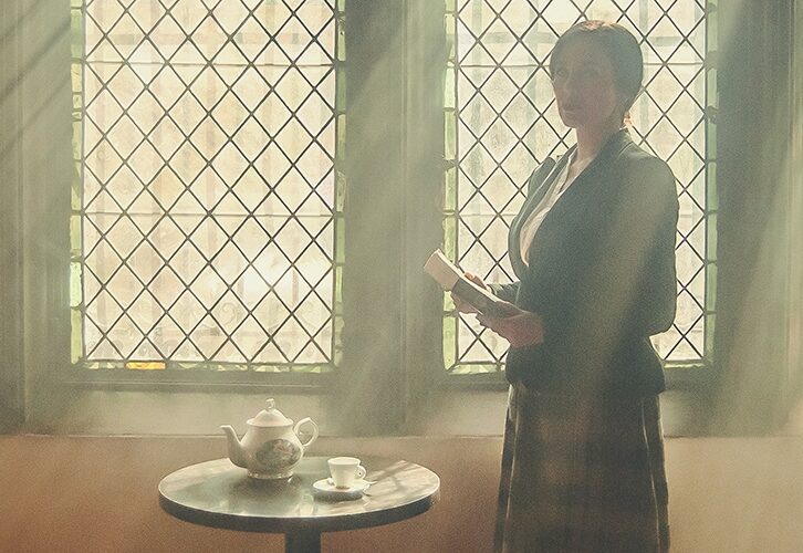 A woman standing by a stained glass window holding a speech she is about to deliver.