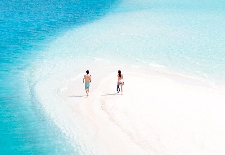 A couple walking on the beach in the Bahamas in their swimsuits for the blog post travel writing tips from a professional editor.