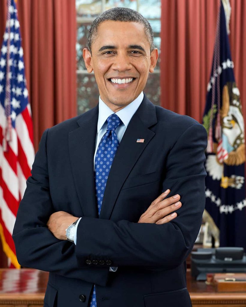 Barack Obama standing with his arms crossed in front of US flag